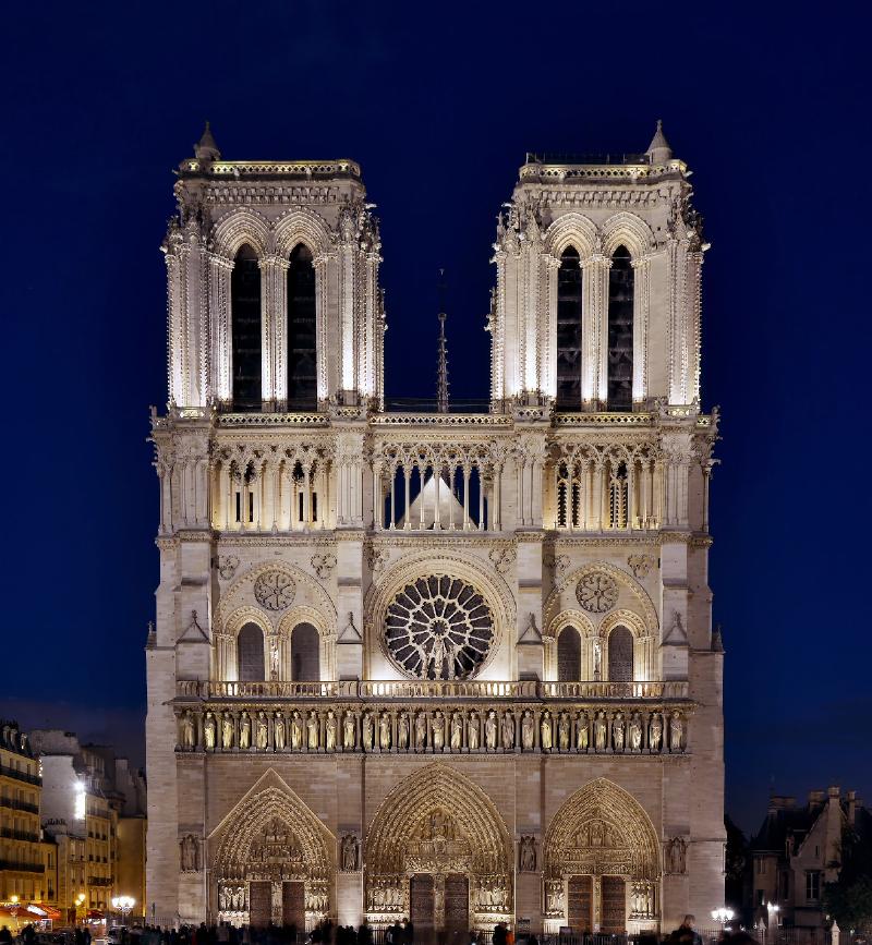 Détails éclairés de la façade de Notre-Dame de Paris la nuit, mettant en valeur les sculptures et rosaces.