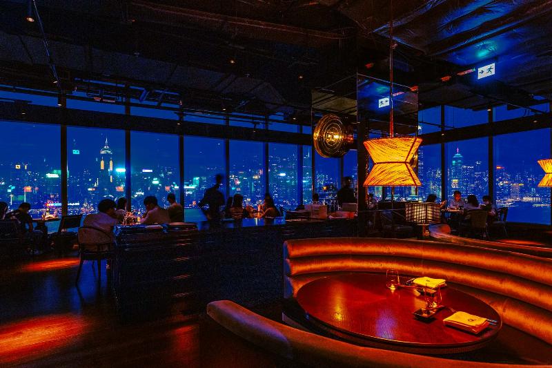 Vue nocturne de la skyline de Hong Kong depuis un rooftop, avec des éléments de culture française au premier plan