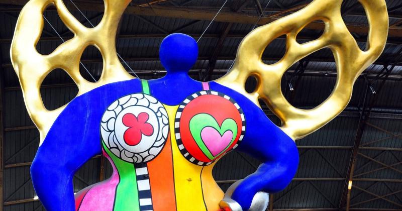 Statue colorée Nana de Niki de Saint Phalle, symbole de joie et de féminité, exposée dans une galerie d'art contemporain.