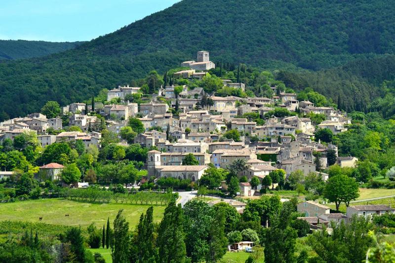 Une peinture détaillée d'un village provençal perché, ses maisons en pierre sous un ciel d'azur