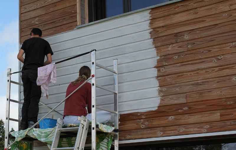 Préparation méticuleuse d'un bardage en bois extérieur avant application de peinture pro
