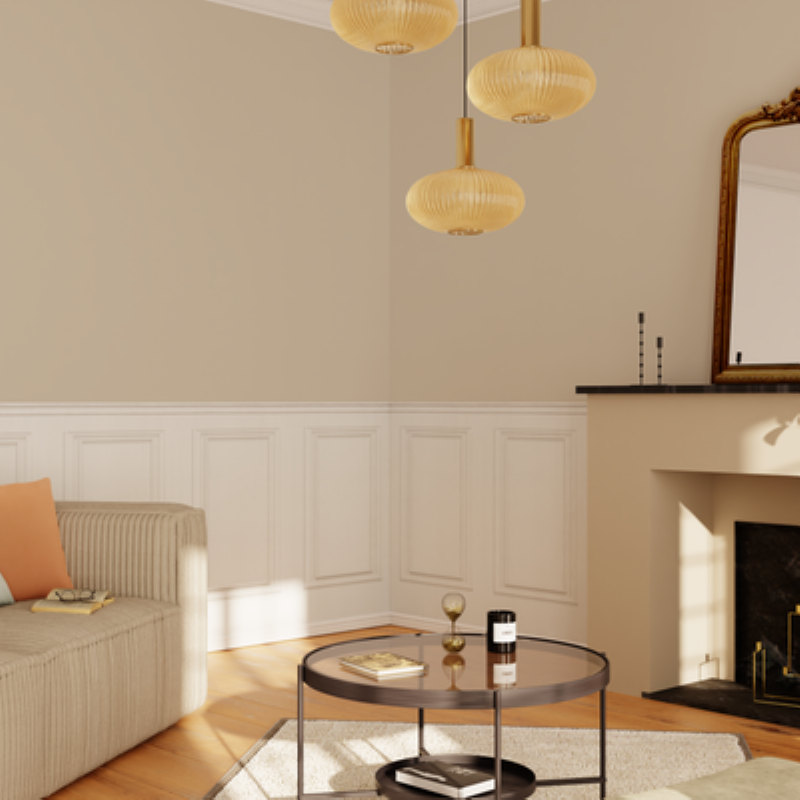 Un salon lumineux aux murs peints en beige sable, avec des moulures classiques et un canapé en lin clair.