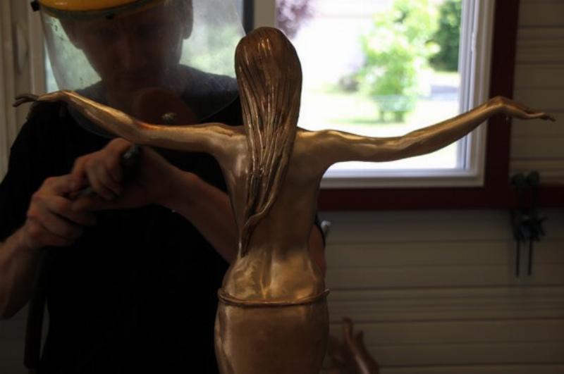 Une sculpture de femme en bronze en cours de finition dans une fonderie d'art, détaillant le travail de la patine
