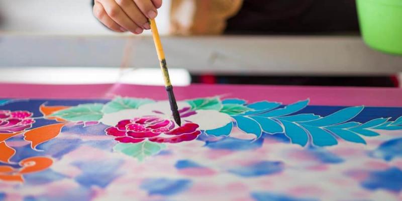 Application minutieuse de peinture textile en bombe à travers un pochoir sur un t-shirt blanc, créant un design géométrique