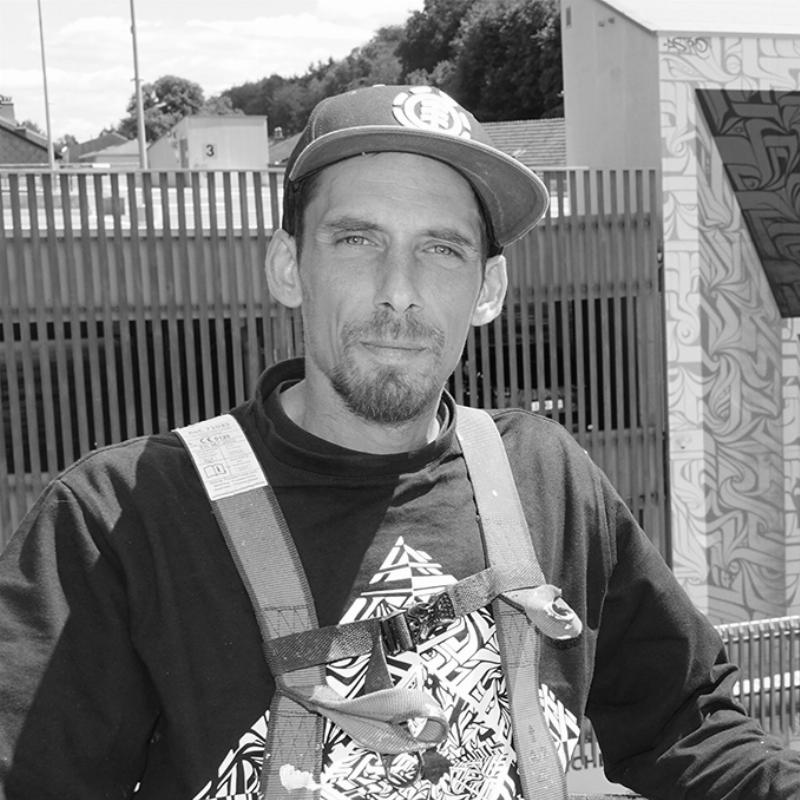 Un artiste au pochoir travaille sur une œuvre d'art urbain détaillée sur un mur de briques, avec des bombes aérosols