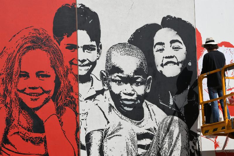 Des artistes de street urbain travaillant sur une grande œuvre murale à Paris, avec des bombes aérosol et des échelles, sous le regard de passants curieux.