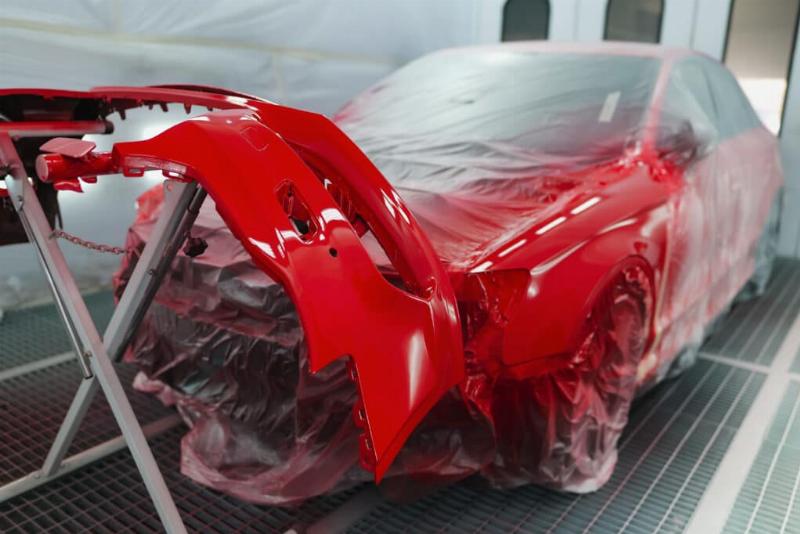 Carrossier expert appliquant une peinture de voiture avec précision dans une cabine