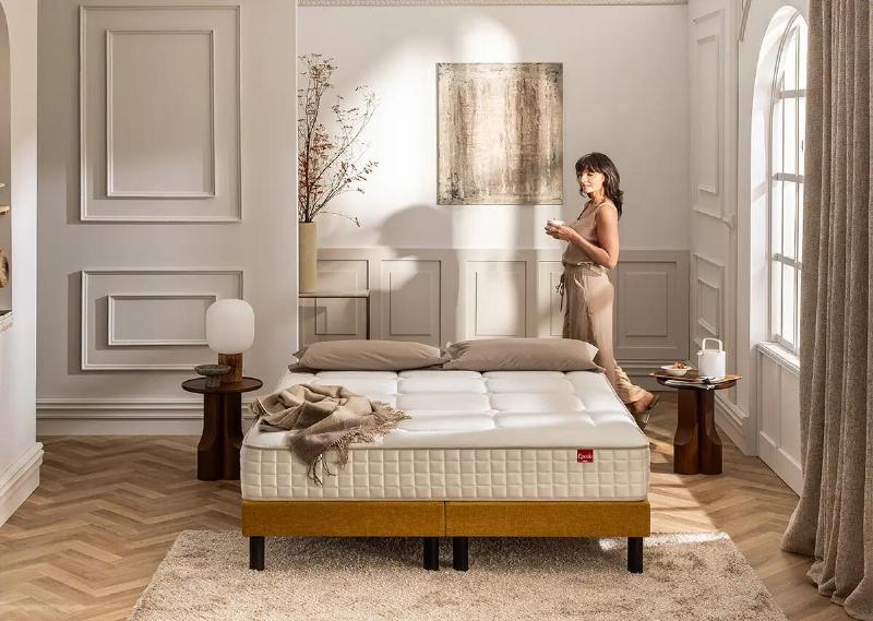 Chambre à coucher élégante avec des murs peints en vert doux, literie grise, mobilier en bois et une touche de décoration française raffinée.