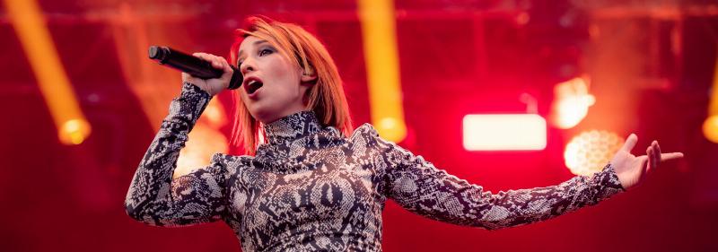 Un chanteur de pop française sur scène, éclairé par des projecteurs colorés, captivant son public avec énergie.