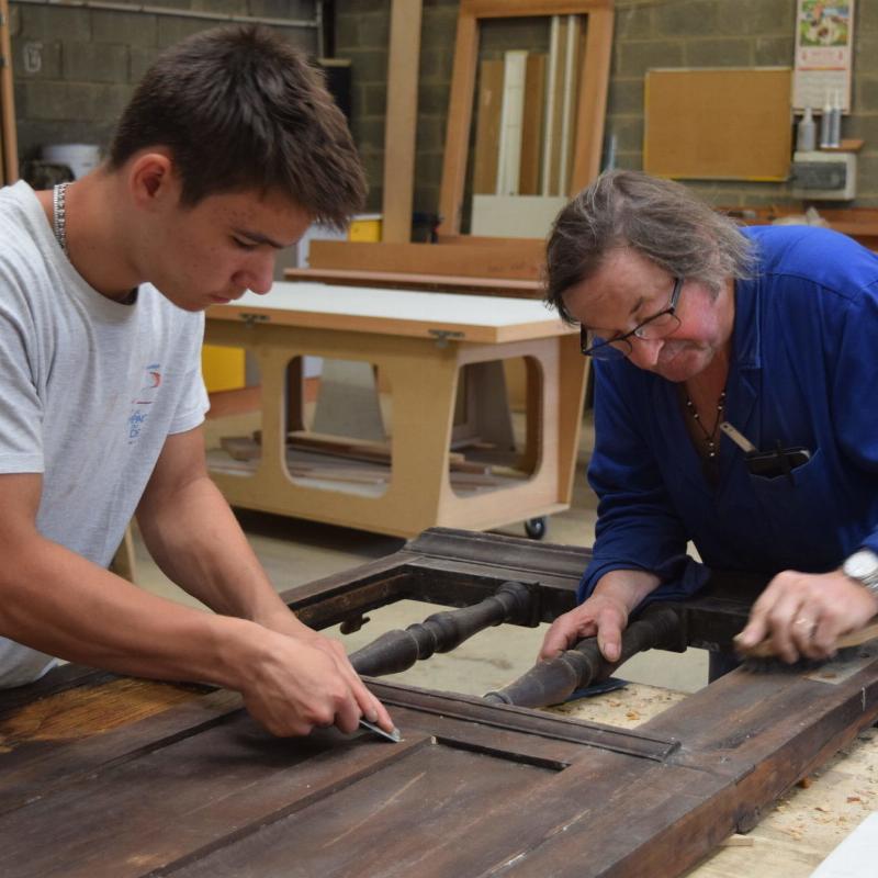 Un chef de chantier de Notre-Dame de Paris partageant son expertise avec de jeunes apprentis artisans, symbolisant la transmission des savoirs sur le chantier de restauration