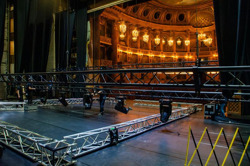 Intérieur d'un château français avec une scène où un orchestre joue, éclairé par des lustres.