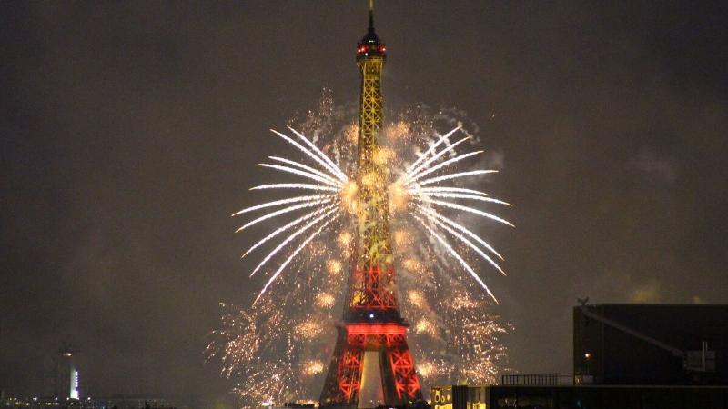 Foule célébrant la Fête Nationale à Paris avec des feux d'artifice sur la Tour Eiffel