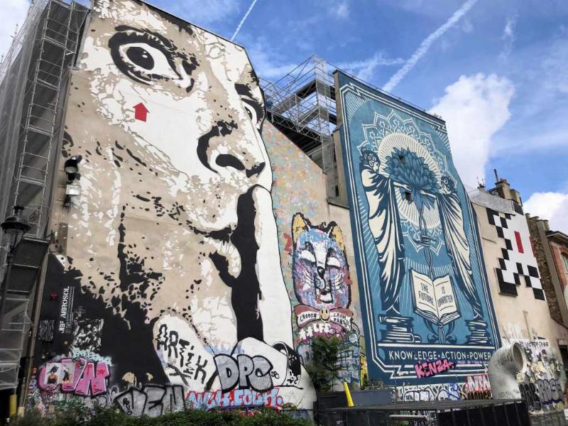 Jef Aérosol, pionnier français du street art, créant une œuvre emblématique au pochoir dans la rue, signature flèche rouge
