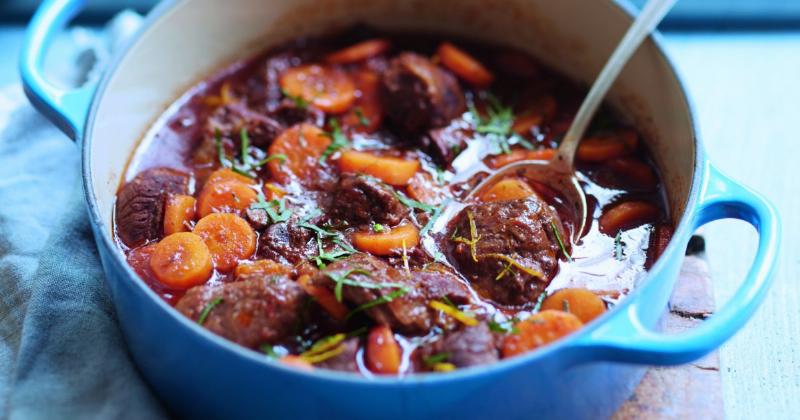 Un chef français préparant un plat traditionnel avec du lard, dans une cuisine rustique et chaleureuse