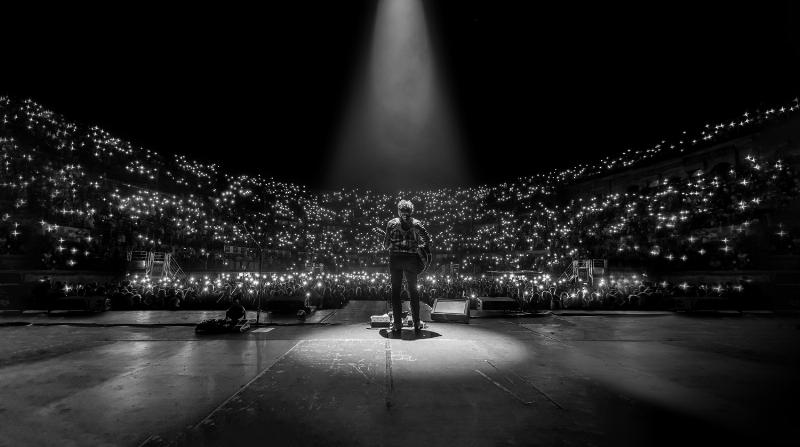Un artiste de chanson pop française sur scène, illuminé par des lumières colorées, chantant avec un micro, le public en arrière-plan flou, capturant l'énergie d'un concert live.