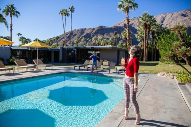 Maison emblématique de l'architecture moderne de Palm Springs, avec de grandes baies vitrées et une piscine, reflétant le ciel bleu