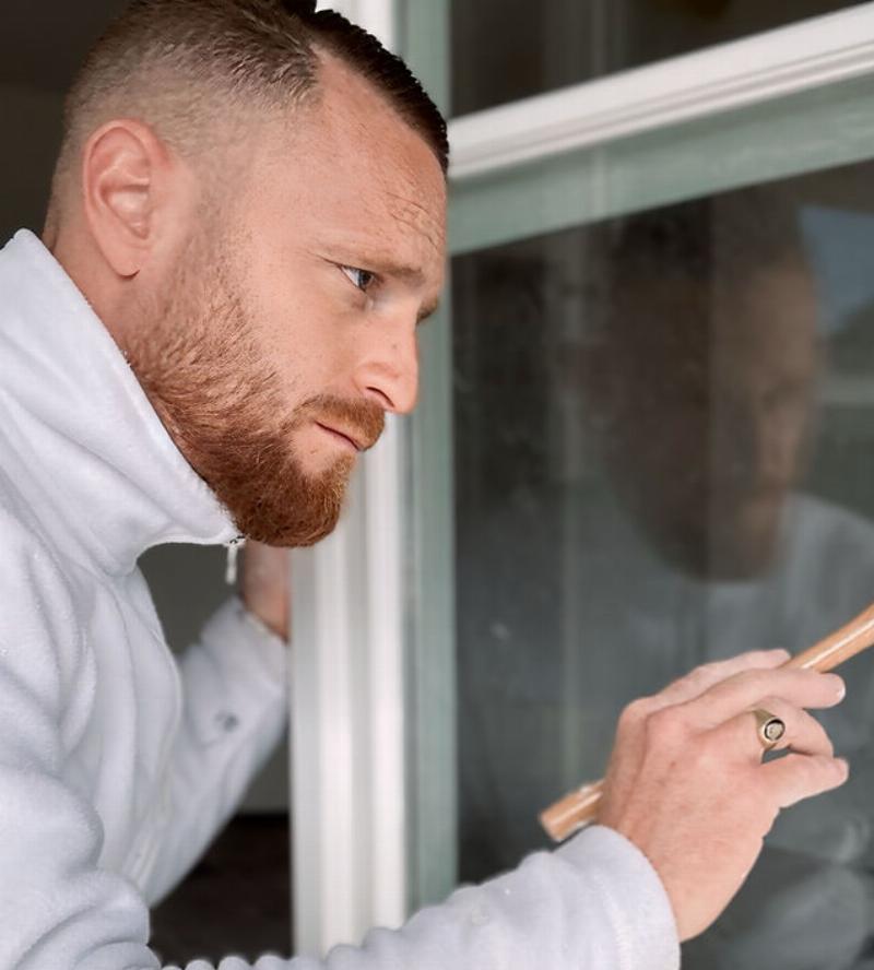 Un artisan peintre appliquant de la peinture sur un volet en PVC extérieur d'une maison traditionnelle française