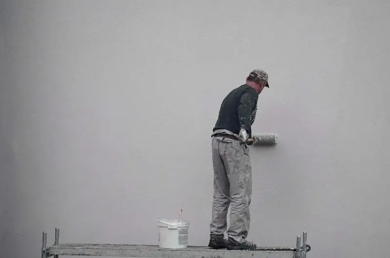 Un peintre expert travaillant sur une façade, entouré de matériaux de qualité pour optimiser le prix au m2 peinture facade.