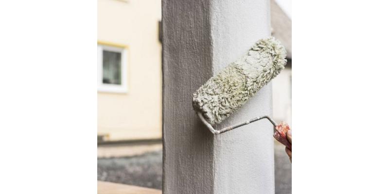 Peintre professionnel appliquant une peinture murale extérieure sur la façade d'une maison ancienne
