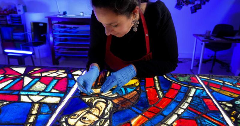 Une restauratrice de vitraux minutieuse travaillant sur un vitrail coloré de Notre Dame de Paris