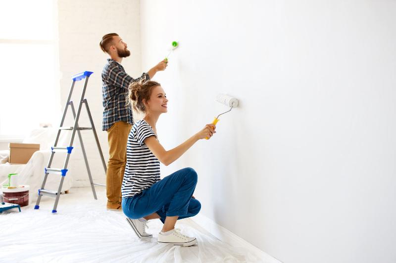 Peintre utilisant un rouleau à peinture avec une perche télescopique pour une application fluide et uniforme sur un mur