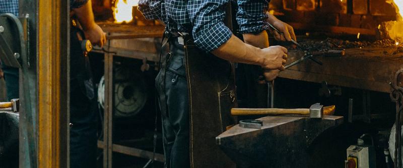 Un sculpteur sur métal travaillant l'acier à la forge, avec des étincelles et des outils traditionnels dans un atelier d'art