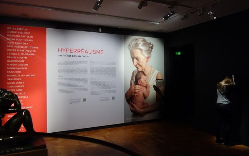 Une sculpture hyperréaliste contemporaine d'une figure humaine assise, montrant des détails incroyablement réalistes de la peau et des vêtements.