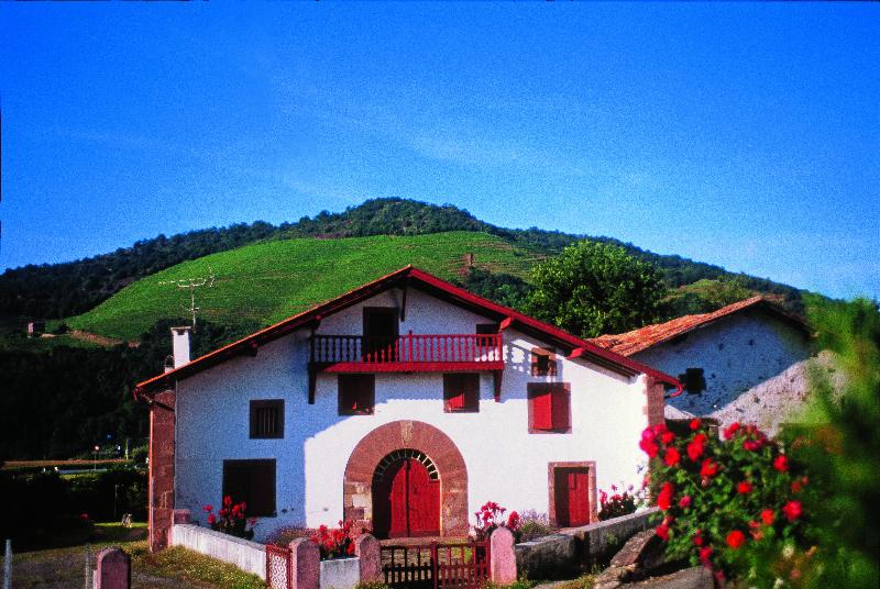 Détail d'une façade de maison basque avec colombages rouges et murs en pierre blanche. 