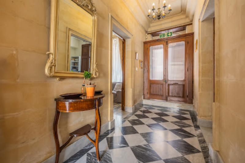 Intérieur lumineux d'une résidence maltaise moderne, avec des meubles épurés, l'utilisation de la pierre calcaire et une grande fenêtre offrant une vue sur la mer.