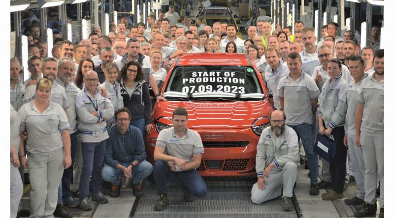 Une jante de voiture en alliage finition gris titane, propre et brillante, reflétant la lumière du soleil, sur un fond flou représentant un paysage automobile élégant.