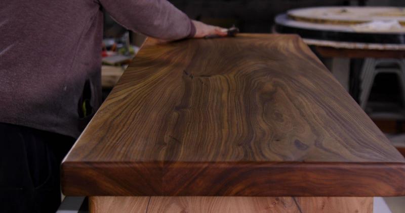 Gros plan sur les mains d'un artisan appliquant une patine sur un meuble en bois, montrant les outils et les couches de peinture et de cire