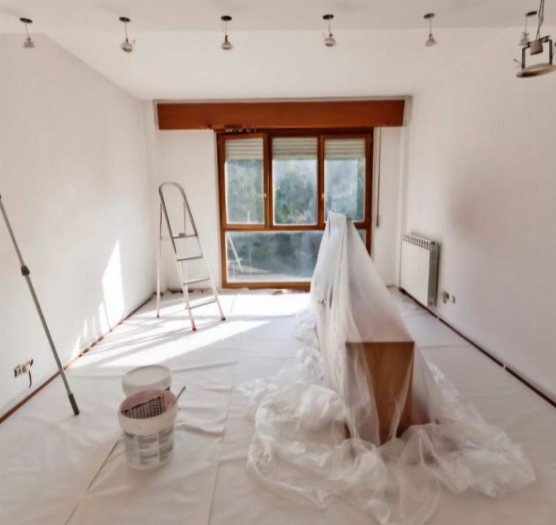 Préparation méticuleuse d'un mur de salon avant l'application de peinture blanche, mettant en avant l'importance des détails pour un fini parfait.