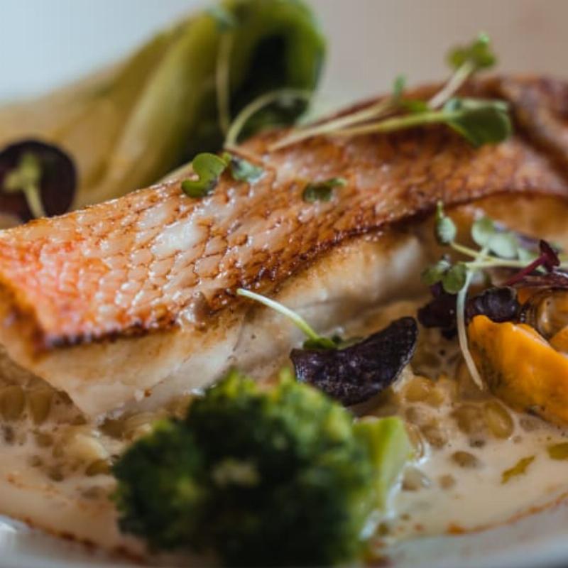 Une maison de campagne française pittoresque avec une façade fraîchement peinte en jaune pâle, entourée de verdure luxuriante et de fleurs colorées.