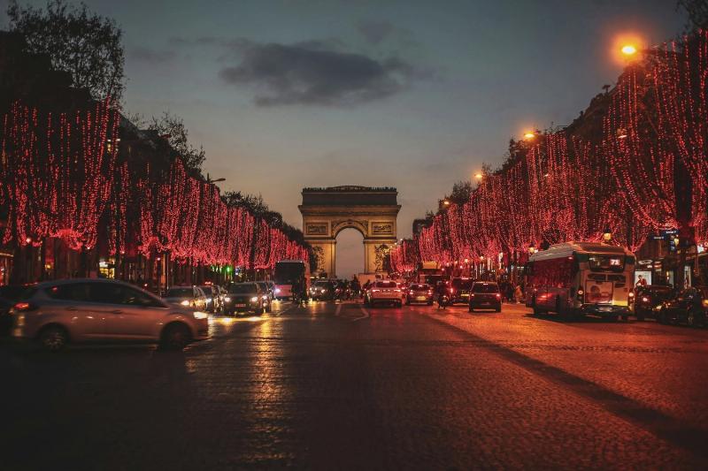 Décoration de Noël dans une rue parisienne animée, illuminée de guirlandes scintillantes et de vitrines festives, ambiance chaleureuse et magique.