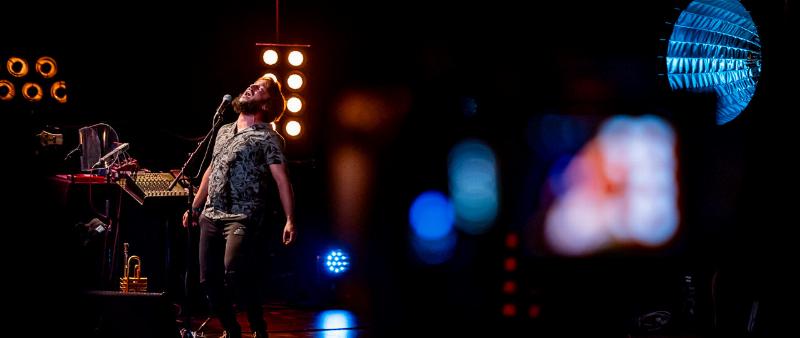 Un concert de musique française avec des lumières vives, une foule enthousiaste et l'artiste sur scène capturant l'énergie du live.