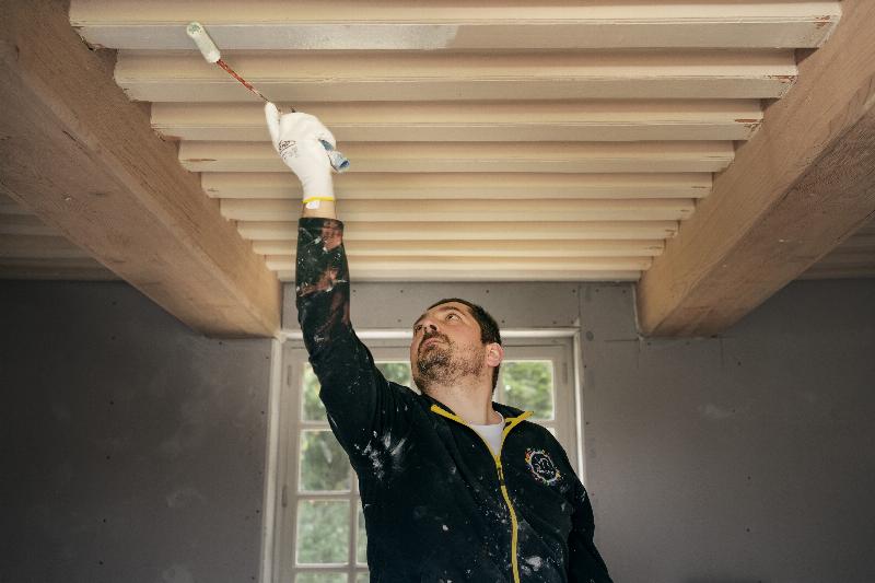 Un artisan français appliqué réalisant une peinture décorative sur un mur ancien, outils à portée de main